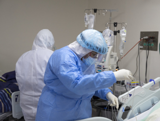 Healthcare worker in PPE prepares patient bed