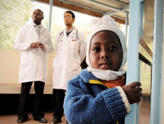 A child and two pediatricians stand near the waiting room at a clinic in Meru District, Kenya. (Photo: Mia Collis/Elizabeth Glaser Pediatric AIDS Foundation)