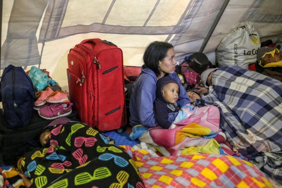 Migrant children and mothers gather with blankets and luggage in a UNICEF tent
